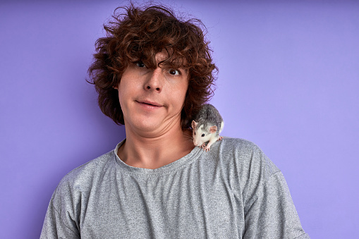 guy makes funny grimace face while his lovely pet rat crawling on him, emotional guy with decorative mouse