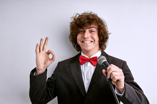 artist in suit with microphone showing OK gesture and smiling, the presentation or speech is good, successful performance