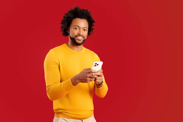 istock Happy handsome young man is using smartphone and texting, messaging in social networks, positive african american guy using mobile app, studio shot isolated on red 1472539865