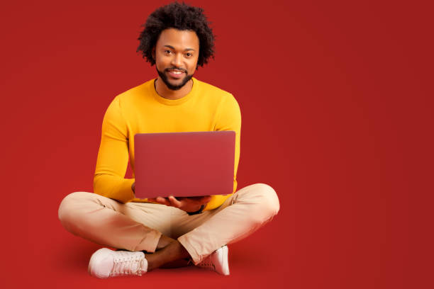 istock Portrait of happy young bearded man holding and using laptop computer isolated on red background. Male office employee typing, answering email 1472539934