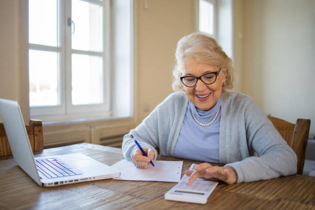 istock Senior woman using calculator while going through bills and home finances 1472540786
