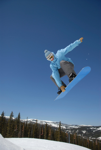 A male snowboarder doing a backside spin over a tabletop jump in a Colorado ski resort's terrain park on a beautiful blue sky day.