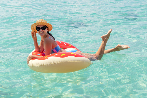 Beautiful young woman with inflatable donut ring relaxing in sea. Summer vacation