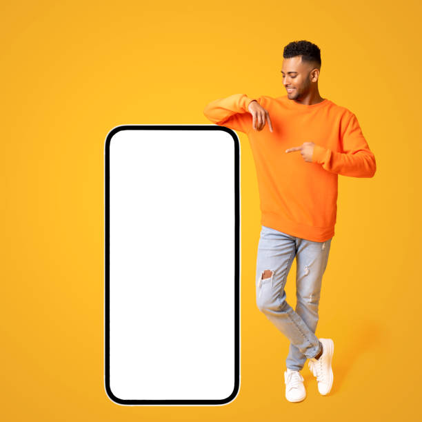istock Optimistic happy indian guy posing by huge smartphone with empty blank screen, pointing at display and smiling 1472546952