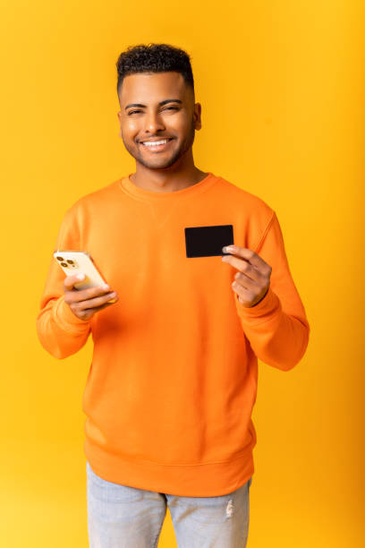 istock Cheerful middle-eastern guy is using smartphone and credit card for shopping online. Happy indian man is ordering food online 1472546969