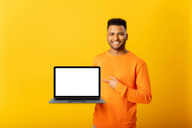 istock Positive optimistic indian guy freelancer or student showing laptop with empty screen and points finger on it 1472547020