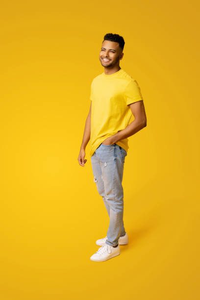 hombre indio complacido en ropa casual se encuentra aislado en amarillo, estudiante masculino, joven guapo de pie - smart casual looking at camera full length indoors fotografías e imágenes de stock