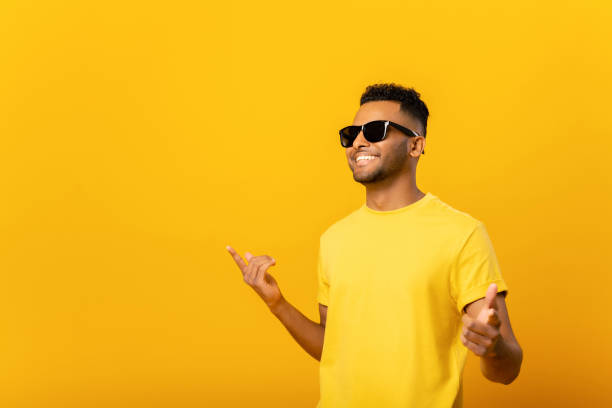 Excited positive young arab man in sunglasses rejoicing, raising hands up and having fun, good mood. Indoor studio shot isolated on orange background stock photo