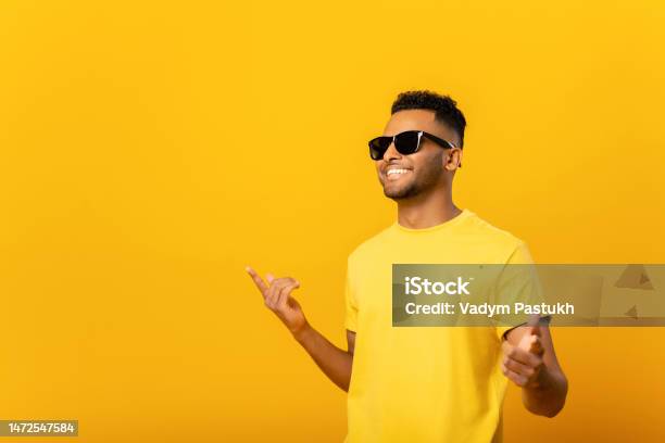 Excited Positive Young Arab Man In Sunglasses Rejoicing Raising Hands Up And Having Fun Good Mood Indoor Studio Shot Isolated On Orange Background Stock Photo - Download Image Now