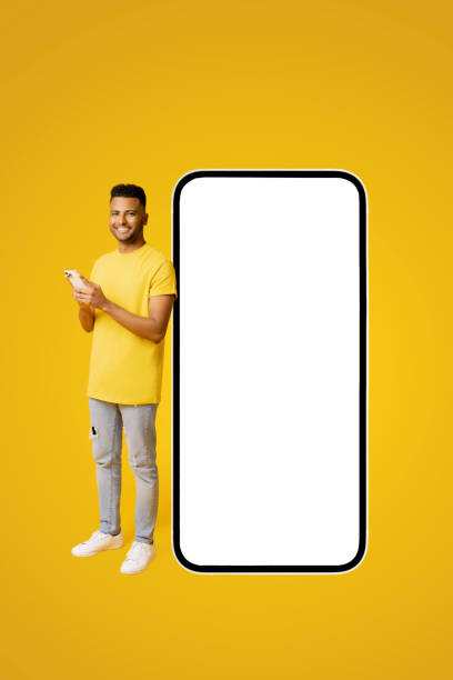 istock Handsome happy indian guy standing near big huge smartphone with blank screen, copy space, mockup, full length 1472547662