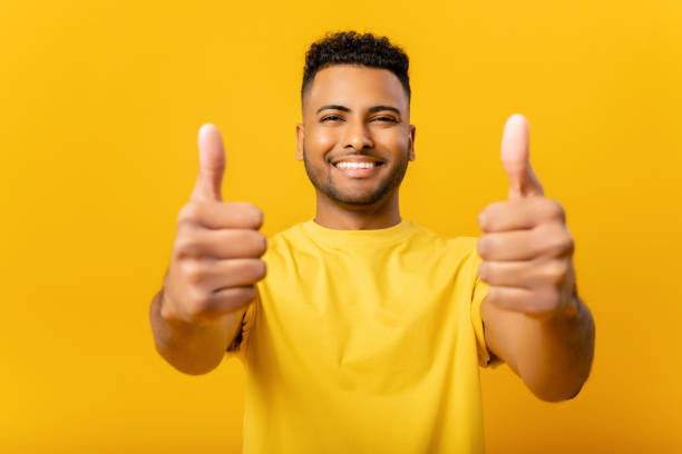Young handsome Indian guy showing thumbs up isolated on yellow