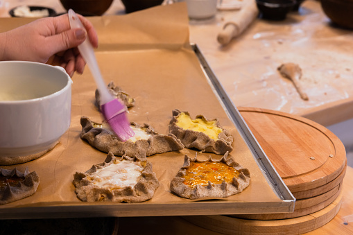 Preparing homemade Karelian pasties for bake, brushing with melted butter, close up photo with selective soft focus