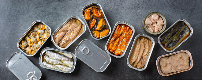 Assortment of different canned preserved fish and seafood in tin cans ready for tinned fish date night. Cheap and lowbrow food during economic crisis and inflation, banner