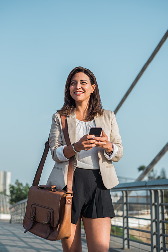 portrait of a businesswoman walking and typing on her cell phone with a smile