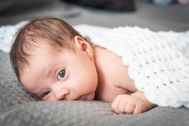 bébé avec boucle d’oreille regardant la caméra allongée avec une couverture sur le lit - boucle doreille photos et images de collection