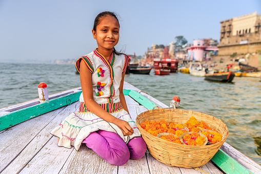 Little girl selling flower candles - a small candles inside a cup made from leaves and flowers. The Ganga is the most sacred river to Hindus.It is worshipped as the goddess Ganga in Hinduism.\nVaranasi is the spiritual capital of India and it is the holiest sacred citiy in Hinduism.