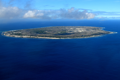 Nauru island: the entire country seen from above - Island surrounded by the coral reef - the oval island has a narrow coastal belt with vegetation where settlements are located, the interior is mostly barren terrain with jagged limestone pinnacles due to the environmental damage caused by phosphate mining - Yaren and the airport on the left - Pacific Ocean -  Pacific Community.