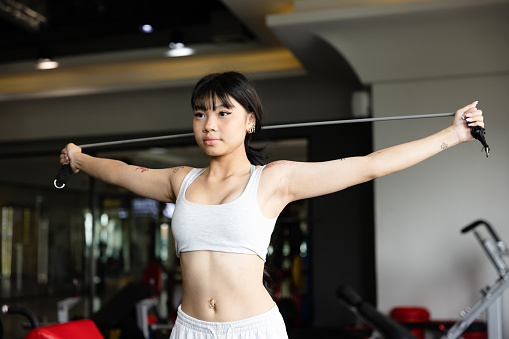 Young Asian woman exercising using stretching rope in gym.