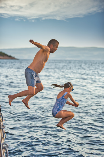 Joyful Father and Daughter on Beach Holiday Jumping from Pier into the Blue Mediterranean Sea