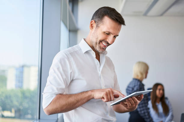 istock Handsome adult businessman standing in office using digital tablet 1472564301