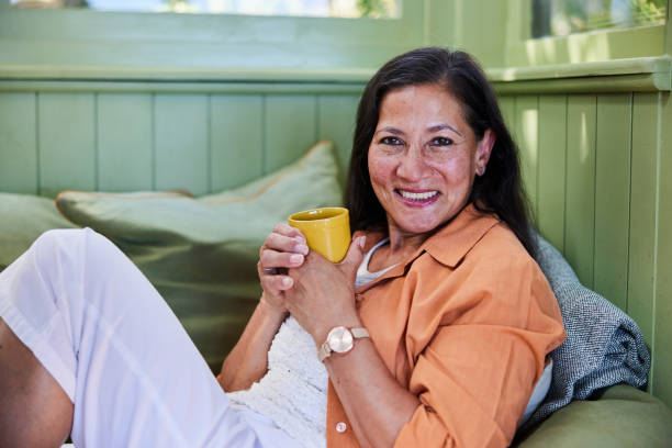 istock Mature woman smiling while drinking coffee on her living room sofa 1472569260