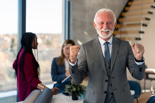 Satisfied senior businessman company CEO standing in front of multicultural team - two business women posing for business portrait, expressing joy because of successful business financial results.