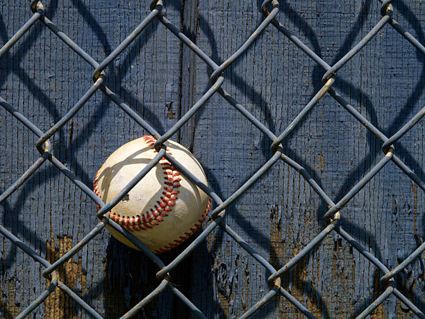 baseball behind fence with shadows stock photo