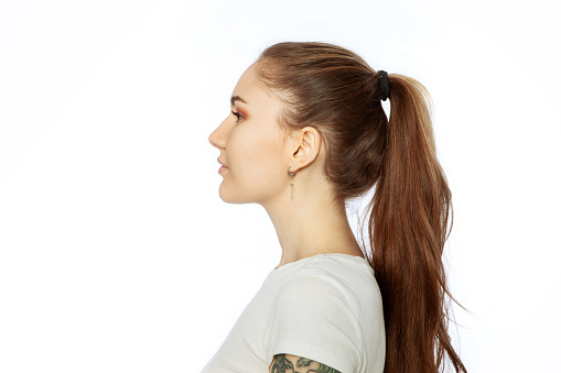 Studio portrait of a young white woman with brown ponytail hair in a white t-shirt against a white background