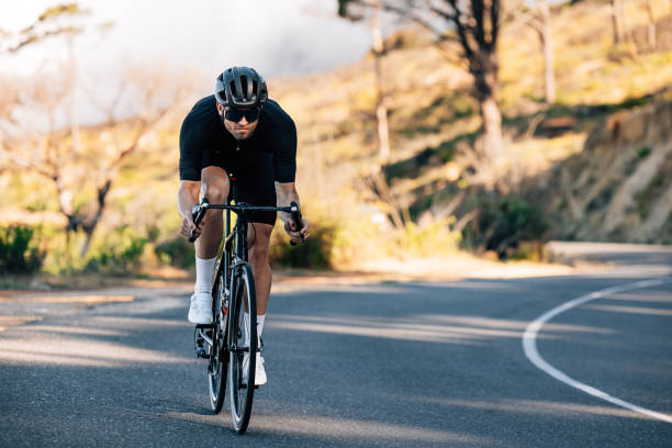 Professional cyclist in black sports attire going down a hill. Cyclist in a helmet and glasses riding on a bicycle outdoors. stock photo