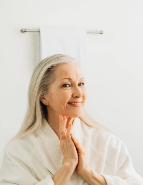 istock Smiling female with grey hair admires her reflection while standing in front of a bathroom mirror in the morning 1472584901