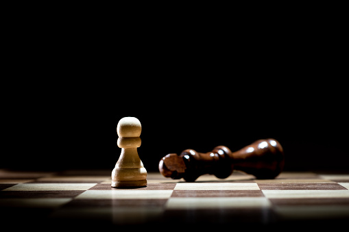 Chess white pawn and black defeated king on black background