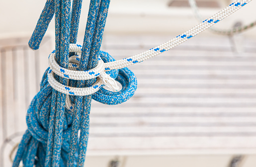 Hanging nautical ropes tied in a knot on a blurred background of the deck of a yacht.