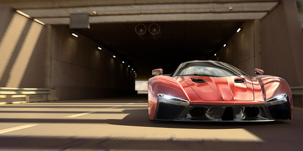 Low angle view of a generic red sports car travelling at speed through a tunnel early in the morning or late in the day. The car has it's headlights on and there is no other traffic on the road.