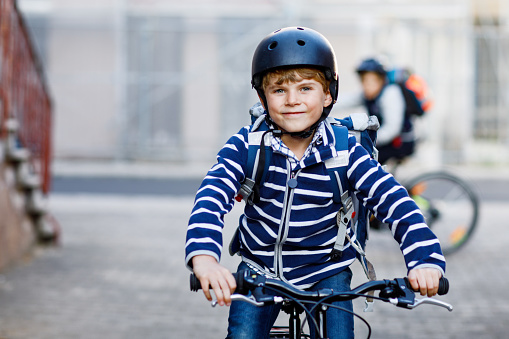 Two school kid boys in safety helmet riding with bike in the city with backpacks. Happy children in colorful clothes biking on bicycles on way to school. Safe way for kids outdoors to school.