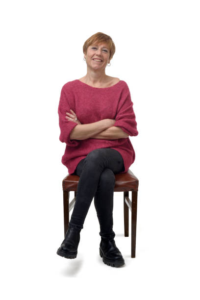 woman isolated on white background front view of a woman in tight jean pants sitting on chair looking at camera and cross legged and arms crossed on white background woman sitting cross legged in chair stock pictures, royalty-free photos & images