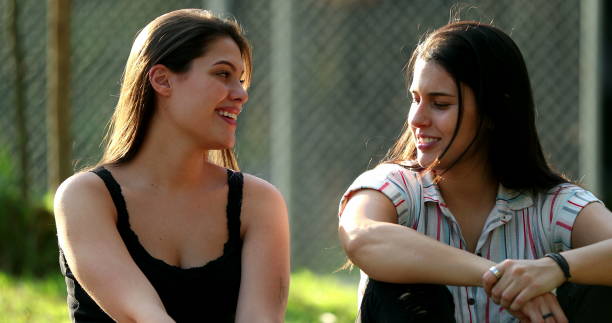 Two female friends speaking outside casually. young women chatting outdoors at park stock photo