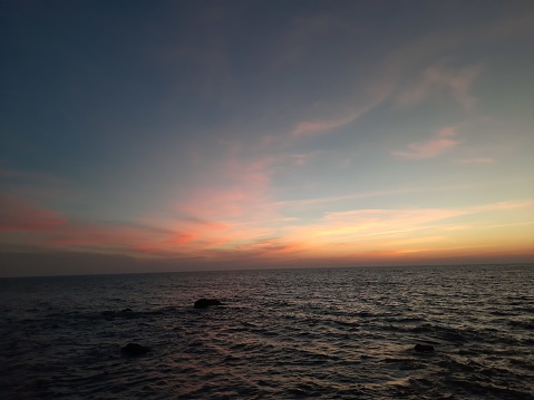 silhouette of a person on the beach, A calm and tranquil zen-like sunset at the beach with beautiful colours in blue and red with reflections on the water.