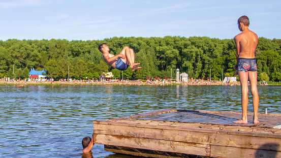 Minsk, Belarus - July 3, 2015: People jump into the water from the pier. Summer fun on the beach