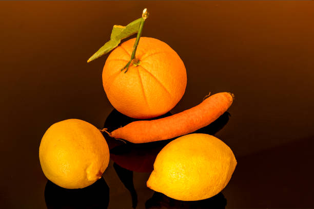composition on a dark background with two lemons a carrot and an orange good to eat and to make juices ace rich in vitamins