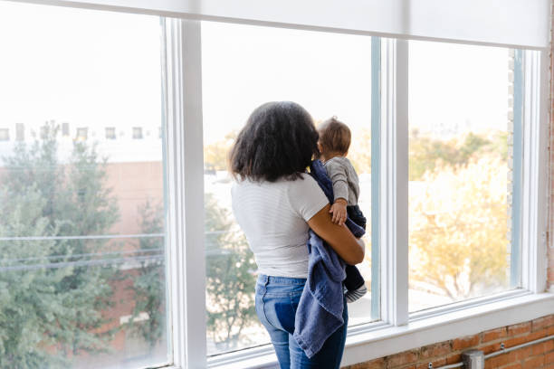 Rear view new mom looking out window with baby son