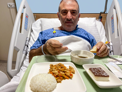 Senior male patient eating foods in hospital bed at hospital room
