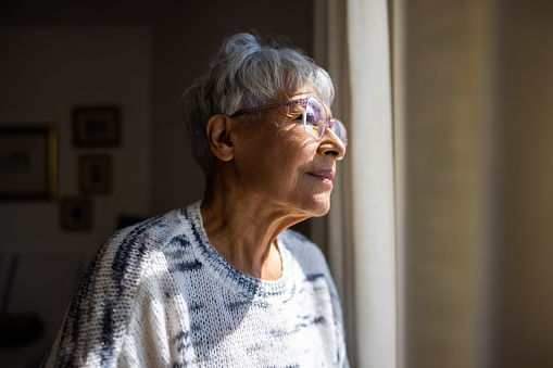 Mujer mayor mirando por las ventanas de su casa photo