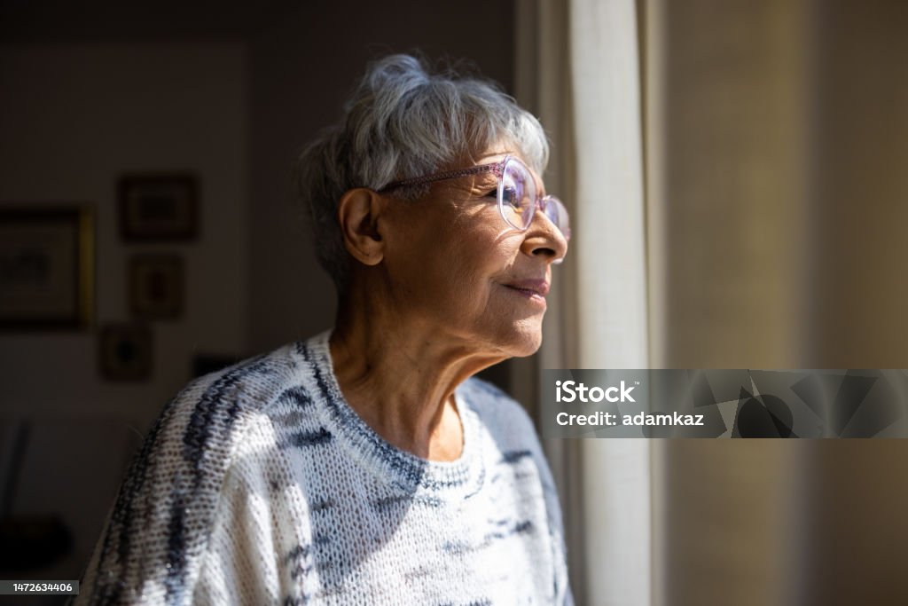 Senior woman looking out the windows of her home A beautiful multiracial senior woman Alzheimer's Disease Stock Photo