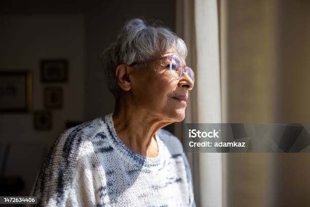 Senior Woman Looking Out The Windows Of Her Home Stock Photo - Download Image Now - Alzheimer's Disease, Senior Adult, Dementia