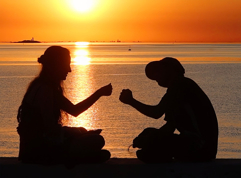 colonia del sacramento, uruguay - november 2 2022: two young people are giving each other a fist bump while enjoying the sunset over the ocean