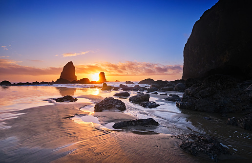 Wintry sun sets behind the Needles at Haystack Rock, Cannon Beach, Oregon, at low tide