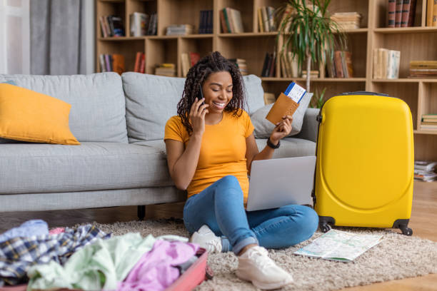 istock Overjoyed black woman using laptop and talking on phone while booking summer trip and preparing for holidays 1472653402