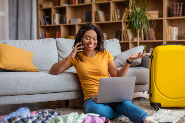 istock Excited african american lady using laptop and talking on phone while searching summer trip, preparing for holidays 1472653421