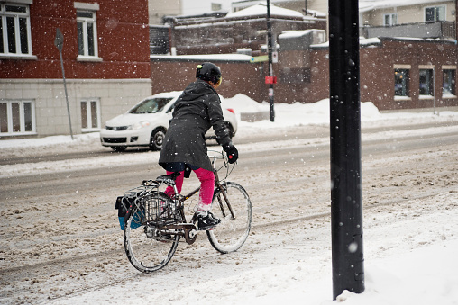 Athletic 50+ woman commuting with bicycle in of the winter snow. She has red hair and is dressed in bright pink and dark gray. Horizontal full lenght outdoors shot with copy space. This was taken in Montreal, Quebec, Canada.