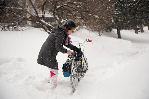 Athletic 50+ woman parking her bicycle in of the winter snow. She has red hair and is dressed in bright pink and dark gray. Horizontal full length outdoors shot with copy space. This was taken in Montreal, Quebec, Canada.